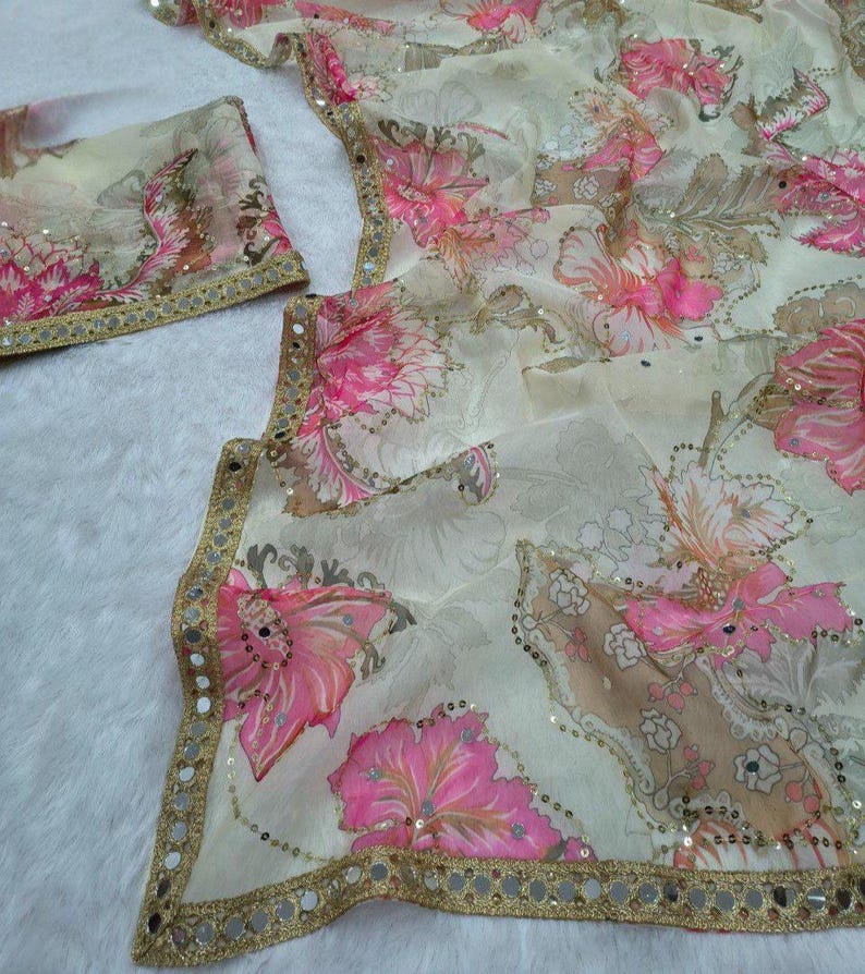 May include: A delicate fabric featuring a floral design in pink and beige hues. It has a gold border with small reflective sequins. The image shows a matching piece, possibly a scarf or accessory, complementing the main fabric.