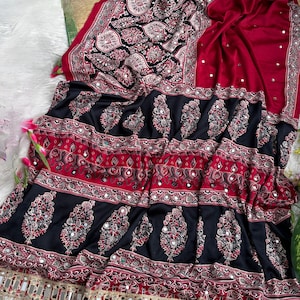 Op de afbeelding: Een dieprode en zwarte stof met ingewikkelde paisley- en bloemmotieven met ingebedde ronde spiegels. Het ontwerp bevat horizontale banden met decoratieve motieven en een onderrand versierd met bungelende metalen spiegelaccenten.