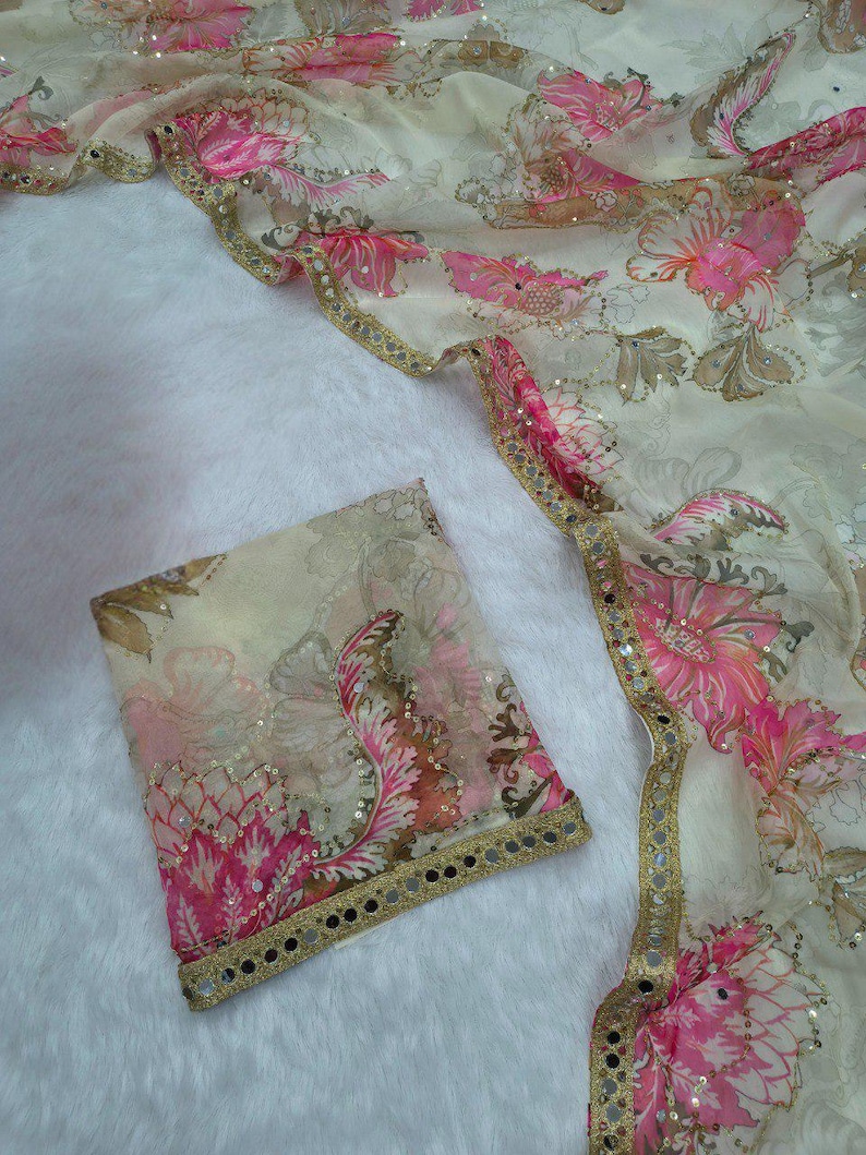 May include: A cream-coloured sheer fabric featuring a pink and brown floral design. The fabric is trimmed with gold and small reflective embellishments. A matching square piece of fabric is also visible.