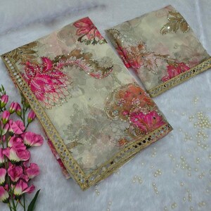 May include: Two-piece floral fabric set with a cream background and pink and brown floral patterns. The edges are trimmed with a gold border. The fabric is decorated with small sequins. The set is placed on a white, fluffy surface.