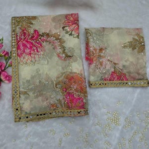 May include: A two-piece floral patterned fabric set. The fabric has a cream background with pink, brown, and orange floral designs. The edges are trimmed with a gold border and small mirrors. The set is likely a scarf and matching fabric.