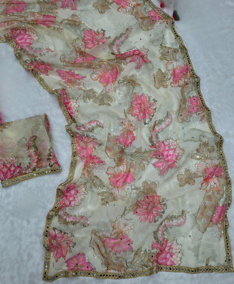 May include: A cream-coloured, sheer fabric featuring a floral pattern in pink and brown. The fabric is embellished with sequins and has a gold-coloured border. A matching piece of fabric is also present.