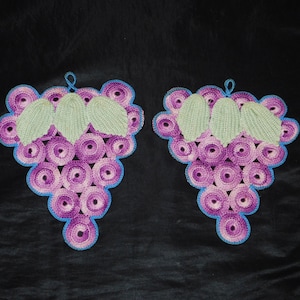 May include: Two crocheted grape designs in purple, pink, and green. The grapes are made of circles and the leaves are made of a textured stitch.