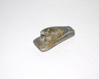 May include: A small, hand-carved stone sculpture of a seal lying on a flat base. The sculpture is made of green and brown stone with black veins.