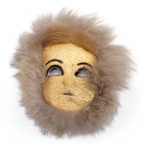 May include: A handmade mask with a painted face and long brown fur trim. The mask has painted eyes and a neutral expression.