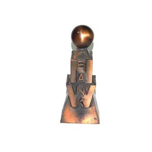 May include: A bronze-colored sculpture with the word "BANK" vertically displayed. The sculpture has a geometric design with a sphere at the top. The letters are in a bold, block style.