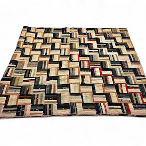 May include: A rectangular quilt featuring a patchwork design composed of numerous small, rectangular fabric strips arranged in a repeating geometric pattern. The quilt displays a diverse color palette including black, white, red, tan, and various shades of green.