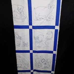 May include: White fabric with a blue grid pattern featuring embroidered animal illustrations. The designs include a cat in a basket, a pig, a rabbit, a bird, a duck, and squirrels. The fabric is hanging from a metal clip.
