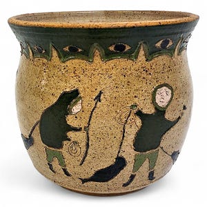 May include: A speckled tan ceramic pot with a dark green rim featuring a repeating eye pattern. The body displays two figures in dark green parkas and light green trousers, one holding a spear and the other a rope, with a black seal-like shape.