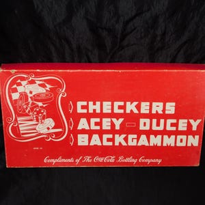 May include: A red box featuring the games Checkers, Acey-Ducey, and Backgammon, with a white graphic of game pieces. The text "Compliments of The Coca-Cola Bottling Company" is printed at the bottom.