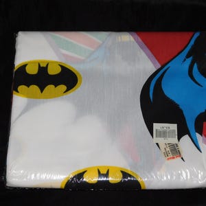 May include: A packaged Batman-themed bed sheet set. The sheets are white with yellow and black Batman logos and a large graphic of Batman's head with a blue cowl. The packaging is clear plastic.