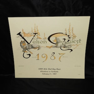 May include: A vintage print featuring the words "Yukon Quest" and "1987" in a stylized font, with illustrations of wolves and trees. The text below reads "1000 Mile Sled Dog Race, Whitehorse to Fairbanks, February 21, 1987."