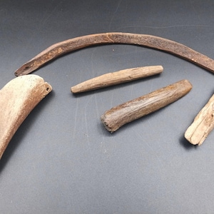 May include: A collection of weathered, brown wooden artifacts. The objects include a curved, boomerang-like piece, a rounded rectangular piece with holes, and several smaller, stick-like pieces. The items appear to be aged and possibly handmade.