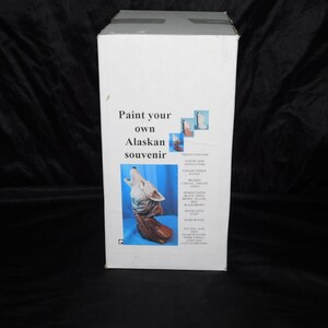 May include: White box with the text "Paint your own Alaskan souvenir." The box features an image of a howling wolf and a list of included items. The box is on a black background.