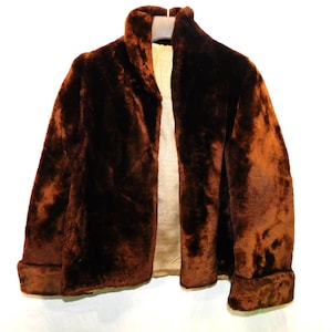May include: A brown faux fur jacket with a shawl collar and folded cuffs. The jacket is open, revealing a light-colored lining. The fur has a rich, textured appearance, and the overall style is vintage.