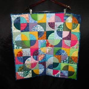 May include: A square patchwork quilt featuring a repeating pattern of multicolored fabric circles. The design consists of various squares in shades of pink, yellow, blue, green, and orange, with diverse floral, striped, and dotted textures.