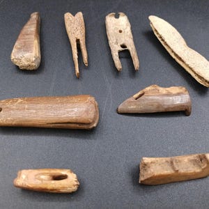 May include: A collection of small, weathered, wooden artifacts. The items include a wedge, a forked piece, a piece with a hole, and a curved, textured object. The objects are various shades of brown and beige, suggesting age and use.