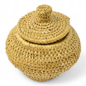 Pode incluir: Uma cesta redonda tecida com uma tampa. A cesta é feita de palha de cor natural e tem uma superfície texturizada. A tampa tem um pequeno botão na parte superior para facilitar a abertura. Esta cesta decorativa é ideal para armazenamento.