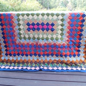 May include: A rectangular quilt featuring a diamond-patterned patchwork design. The quilt is composed of numerous small fabric squares in various colors including blue, red, green, brown, pink, and floral prints, finished with a solid blue border.
