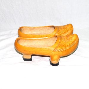 May include: A pair of wooden clogs with intricate carvings. The clogs are a light brown color and have a rounded toe.