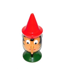 Op de afbeelding: Houten eierdopje in de vorm van een kabouter met een rode hoed, zwart haar en een lange neus. Het eierdopje heeft een groene basis en is beschilderd met gezichtsdetails.