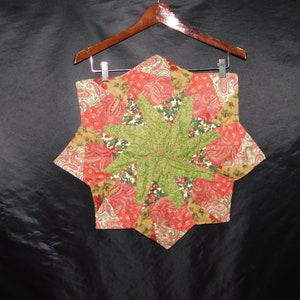 Könnte beinhalten: Ein sternförmiger, gesteppter Tischläufer in Grün, Rot und Gold mit Paisley-Muster.