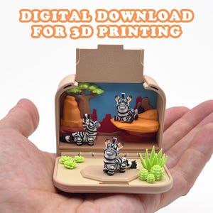 May include: A beige, open, box-like structure containing three small zebra figurines, orange rock formations, a green tree, and green succulents. The text "DIGITAL DOWNLOAD FOR 3D PRINTING" is displayed in orange letters above the object.