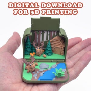 May include: A 3D printed digital download file featuring a miniature diorama inside an olive green case. The scene depicts a forest with two brown moose, a log cabin, green pine trees, a blue stream, gray rocks, and a small green fern plant.