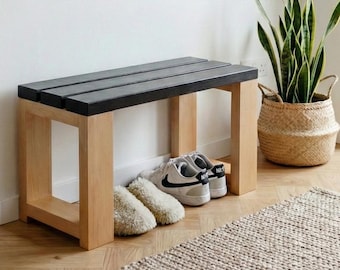 May include: A modern entryway with a wooden bench with a black top, a round mirror, and a denim jacket hanging on a wooden rack. A woven basket holds a tall green plant, and a small rug sits on the floor.