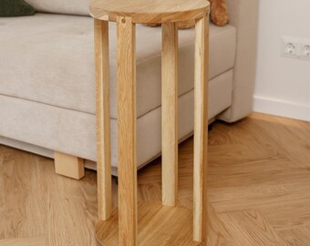 Könnte beinhalten: Ein helles Holz-Beistelltisch mit einer runden Oberseite und vier vertikalen Beinen. Der Tisch ist aus Naturholz gefertigt und steht auf einem Holzboden. Ein Teddybär und Kissen befinden sich auf dem beigen Sofa im Hintergrund.