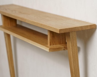 May include: A light oak wood console table with a minimalist design. The table features a long, rectangular top with a lower shelf and angled legs. The natural wood grain is visible, and the table is set against a neutral wall.