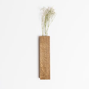May include: A rectangular wooden vase with a natural wood grain. It contains a small arrangement of delicate white flowers. The design is minimalist and modern, suitable for home decor.