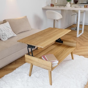 May include: A light-colored wooden lift-top coffee table with a lower shelf, resting on a white fluffy rug. The table is in the raised position, revealing a storage space. Two books are visible on the lower shelf. The table is in a living room setting.