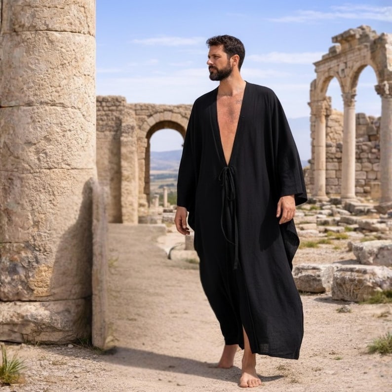 May include: A black, long-sleeved robe with a deep V-neck and tie closure. The robe is made of a lightweight fabric and falls to the ankles. The background features ancient ruins and a blue sky.