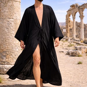 May include: A black, long, open-front robe with wide sleeves and a tie closure at the waist. The robe is worn outdoors, with ancient ruins and a blue sky in the background. The robe is made of a lightweight fabric.