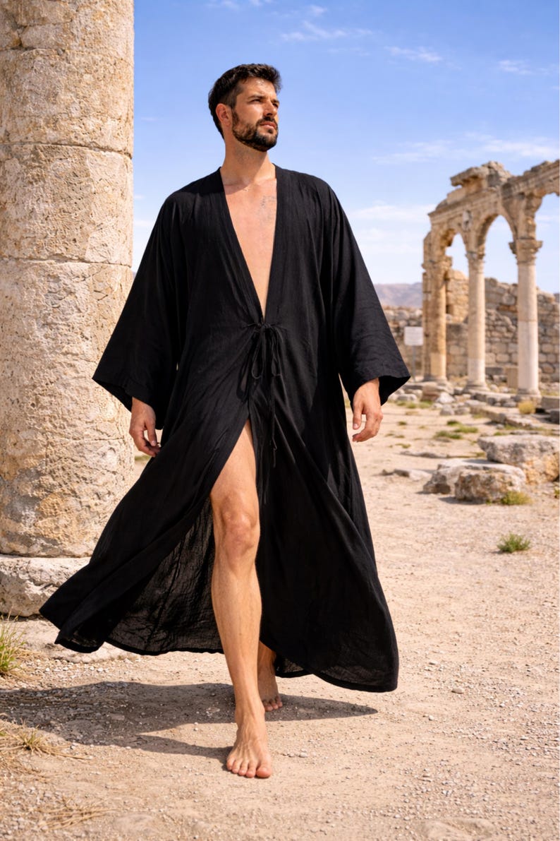 May include: A black, long, open-front robe with wide sleeves and a tie closure at the waist. The robe is worn outdoors, with ancient ruins and a blue sky in the background. The robe is made of a lightweight fabric.