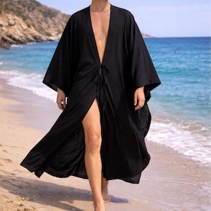 May include: A black, open-front robe with wide sleeves, tied at the waist. The robe is knee-length and worn on a beach with the ocean in the background. The fabric appears lightweight and flowing.