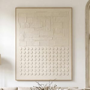 May include: A large, rectangular abstract wall art piece with a light beige color. The top section features a textured, brick-like pattern, while the bottom half has a grid of raised circles. The artwork is framed in a light wood.