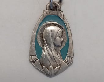 May include: Silver pendant featuring a profile of a woman with a veil, set against a teal background. The pendant has a detailed design and a loop for a chain. Religious jewelry.