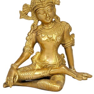 Può includere: Una statua color oro di una figura seduta con dettagli ornati. La figura indossa un copricapo e gioielli dettagliati, con braccia e gambe in posa rilassata. La statua è realizzata in un materiale metallico lucido.
