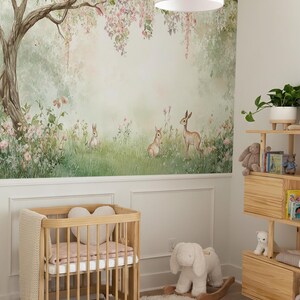 May include: A nursery featuring a light wood crib, a white rug, and a wall mural of a forest scene with deer and rabbits. A wooden bookshelf holds books and soft toys. A white rocking bunny sits on the floor.