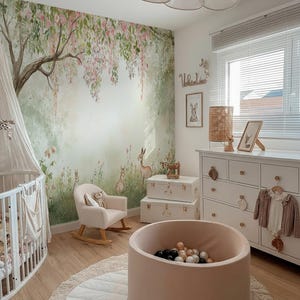 May include: A child's nursery featuring a forest mural, a white cot, and a pink rocking chair. A ball pit with black and white balls is on a round rug. A white chest of drawers and storage trunks complete the room's decor.