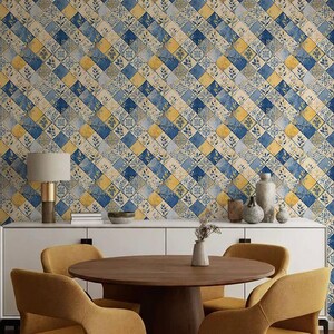 Puede incluir: Un comedor con una mesa redonda de madera y cuatro sillas de color mostaza. La pared está cubierta con un papel pintado estampado con baldosas cuadradas azules, amarillas y crema. También se ven un mueble blanco y objetos decorativos.