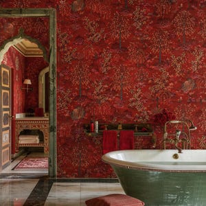 May include: A luxurious bathroom with red floral wallpaper and a green bathtub. The wallpaper features a repeating pattern of trees and flowers. The bathroom also includes a vanity, towels, and a decorative archway.