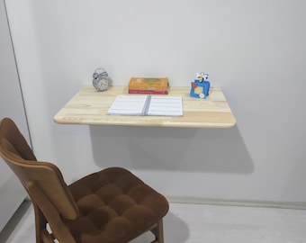 May include: A light-colored wooden wall-mounted desk with a small alarm clock, books, and a notebook. A brown chair with a tufted seat is in front of the desk. A small blue decorative item is on the desk.