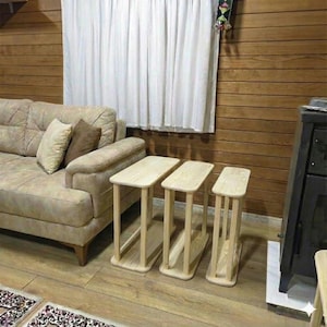 May include: Three wooden side tables of varying heights. Each table has a rectangular top and four supporting legs. The tables are made of light-colored wood and are arranged in a row. The tables are placed on a wooden floor.