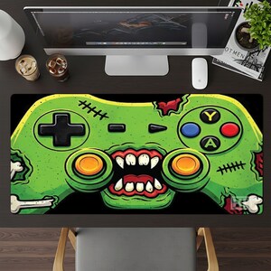 May include: A black gaming mousepad featuring a green zombie-themed game controller design. The controller has a cross-shaped directional pad, buttons in blue, red, and yellow, and a zombie mouth graphic. The mousepad is rectangular.