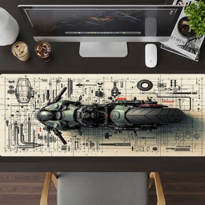 May include: A desk mat featuring a detailed illustration of a motorcycle, rendered in shades of green, gray, and black, set against a blueprint-style background. The mat is rectangular and designed to fit under a computer setup.