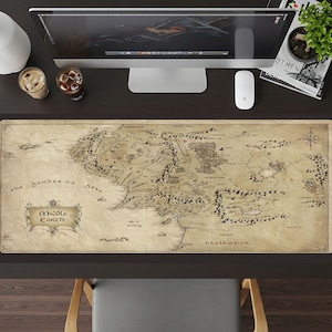 May include: A large, rectangular desk mat featuring a detailed map of Middle Earth. The map is in shades of brown and beige, with intricate drawings of mountains, forests, and bodies of water. The words "Middle Earth" are displayed in a decorative banner.