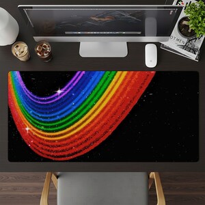 May include: A rectangular desk mat featuring a vibrant rainbow design against a black background. The rainbow arcs across the mat, with colors transitioning from red to orange, yellow, green, blue, and purple. Two white stars add a touch of sparkle.